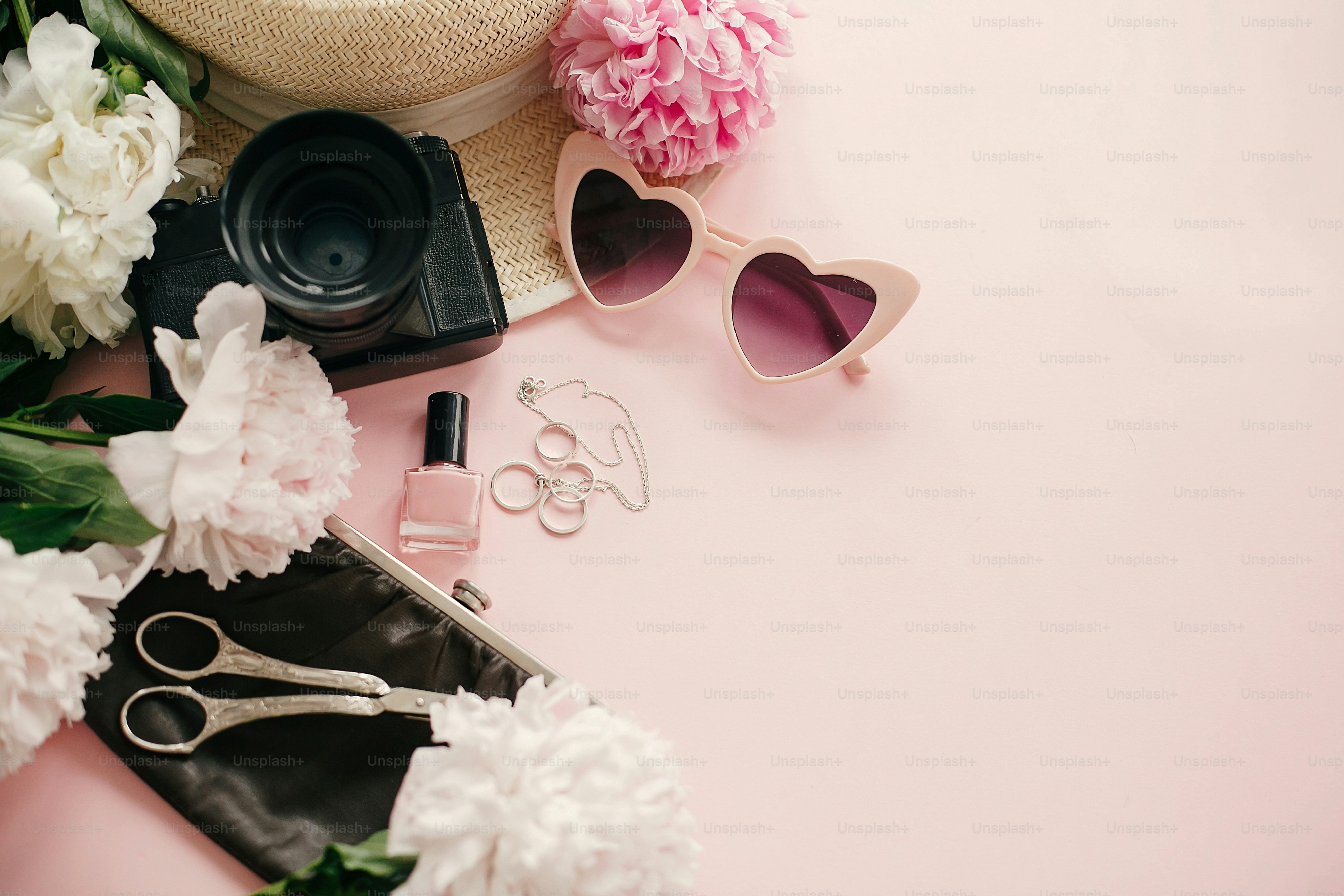 Peonies, camera, heart-shaped sunglasses, and accessories on a soft pink background