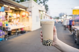 若い女性が台湾の夜市で黒糖タピオカミルクティーのプラスチックカップを持っている、台湾の珍味、クローズアップ。