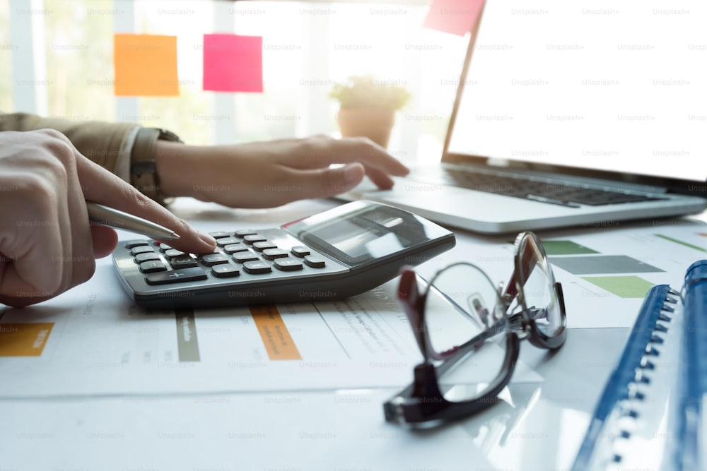 Close up of businessman or accountant hand holding pencil working on calculator to calculate financial data report, accountancy document and laptop computer at office, business concept