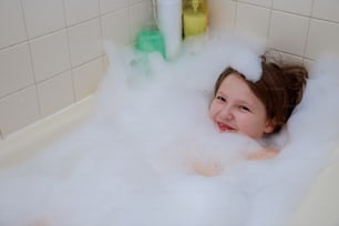 Bambino felice nella vasca da bagno, nuotando nella schiuma. Doccia bambino.
