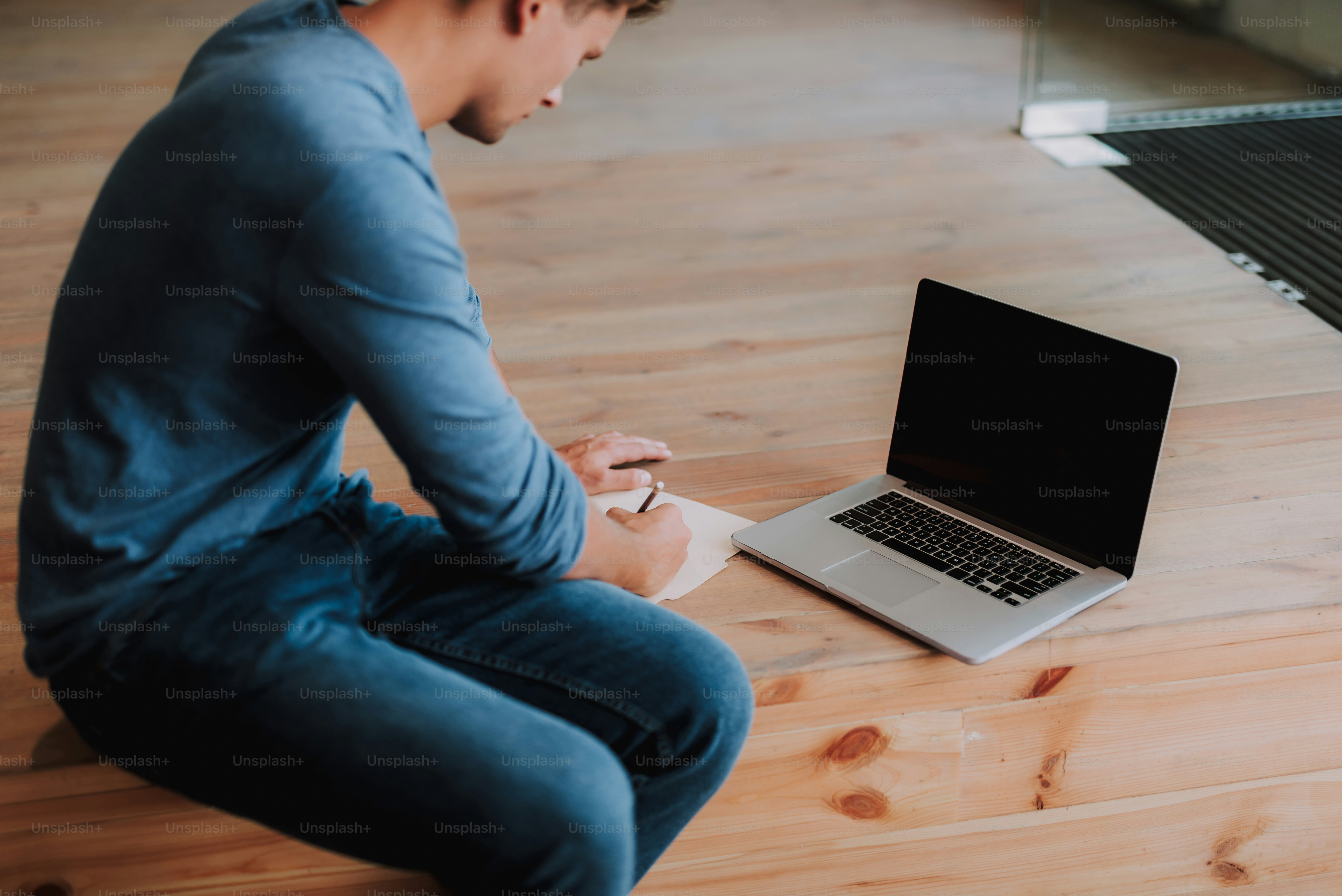 Tampilan atas desainer terkonsentrasi membuat catatan di notebook saat menggunakan laptop