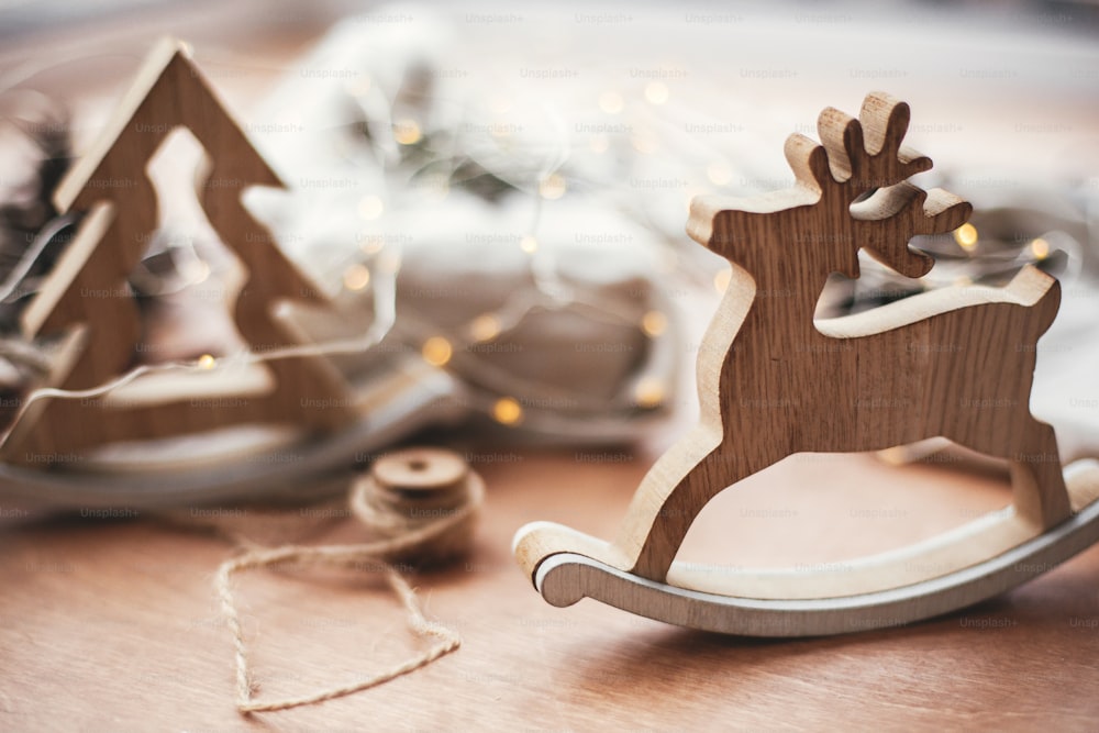 Juguete navideño rústico de reno sobre mesa de madera sobre fondo de árbol de madera, luces, cordel, regalo en tela de lino con rama verde, piñas. Regalos ecológicos sencillos. Vacaciones residuo cero