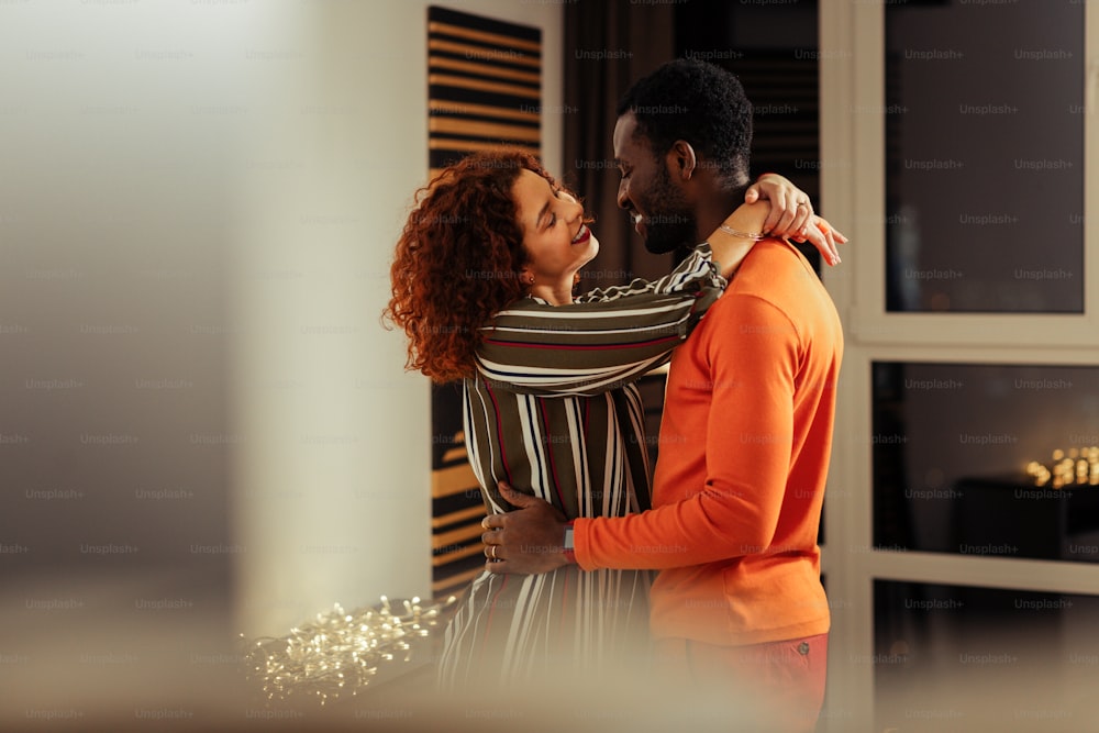 Appealing girlfriend. Handsome African-American boyfriend hugging his appealing girlfriend