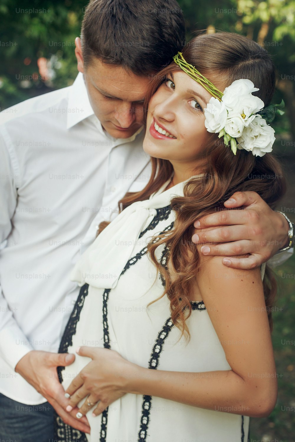Responsible husband hugging beautiful stylish wife in retro white dress with flowers in her hair, famiy portrait