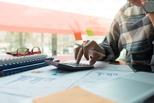 Un homme travaillant sur le document d’affaires financier et d’analyse avec une calculatrice et tenant des lunettes à son bureau pour calculer les dépenses, concept de comptabilité