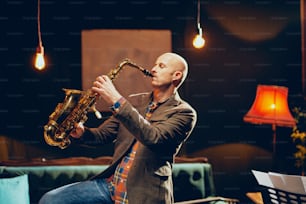 Young talented saxophone player playing his instrument and standing in home studio.