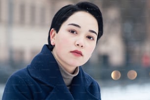 Nahaufnahme Porträt einer brünetten jungen Frau mit kurzen Haaren, die im Winter einen blauen Mantel im Freien trägt.