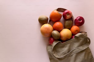 Cotton bag with different fruits on pink background. Ecology pack for free plastic shopping. Top view. Flat lay