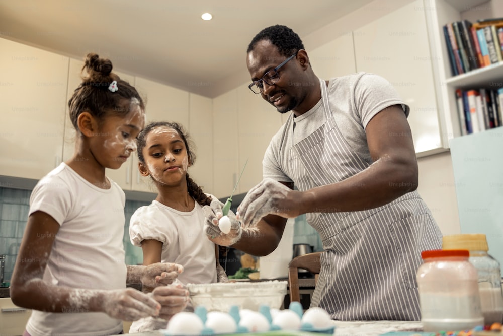 Cupcakes with father. Funny dark-haired daughters cooking cupcakes with father wearing striped apron