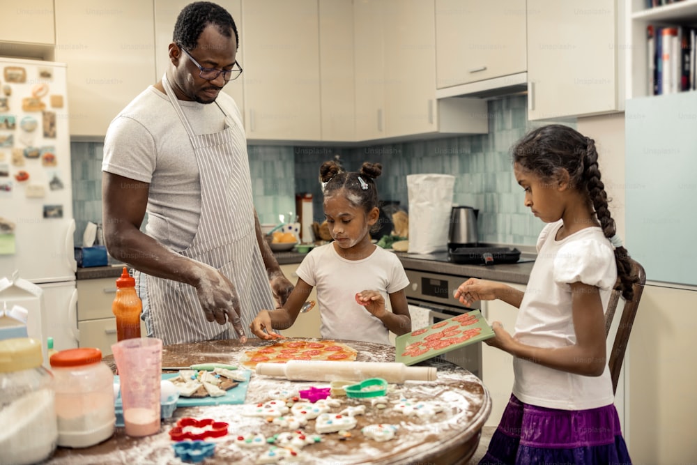 Pizza mit Salami. Vater und zwei hilfsbereite kleine Töchter kochen Pizza mit Salami zum Mittagessen