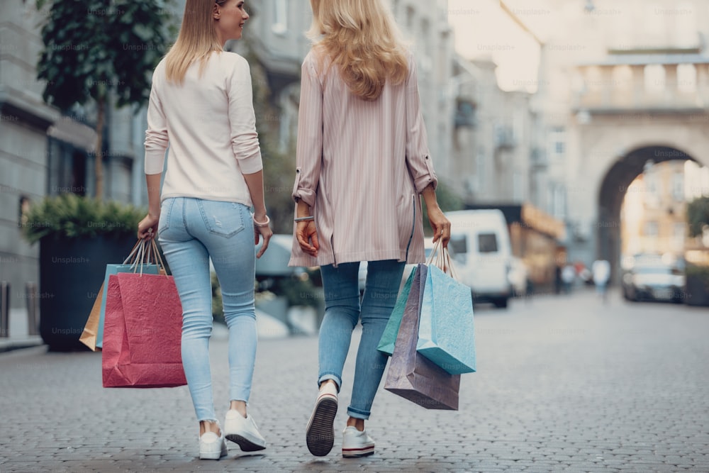 Cropped back view portrait of beautiful girl chatting with mother after shopping. They holding colorful paper bags
