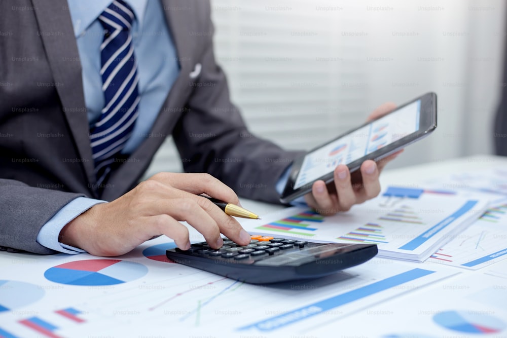 Close up businessman using calculator and tablet in the calculations revenue and market statistics.