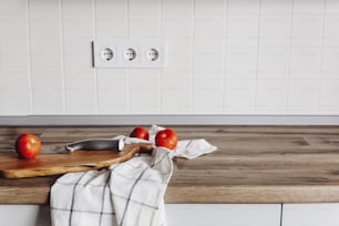Cuisson des aliments dans une cuisine moderne, couteau sur une planche à découper en bois avec des légumes, épices sur une table en bois. Nourriture maison. Meubles de cuisine élégants de couleur grise dans le style scandinave.