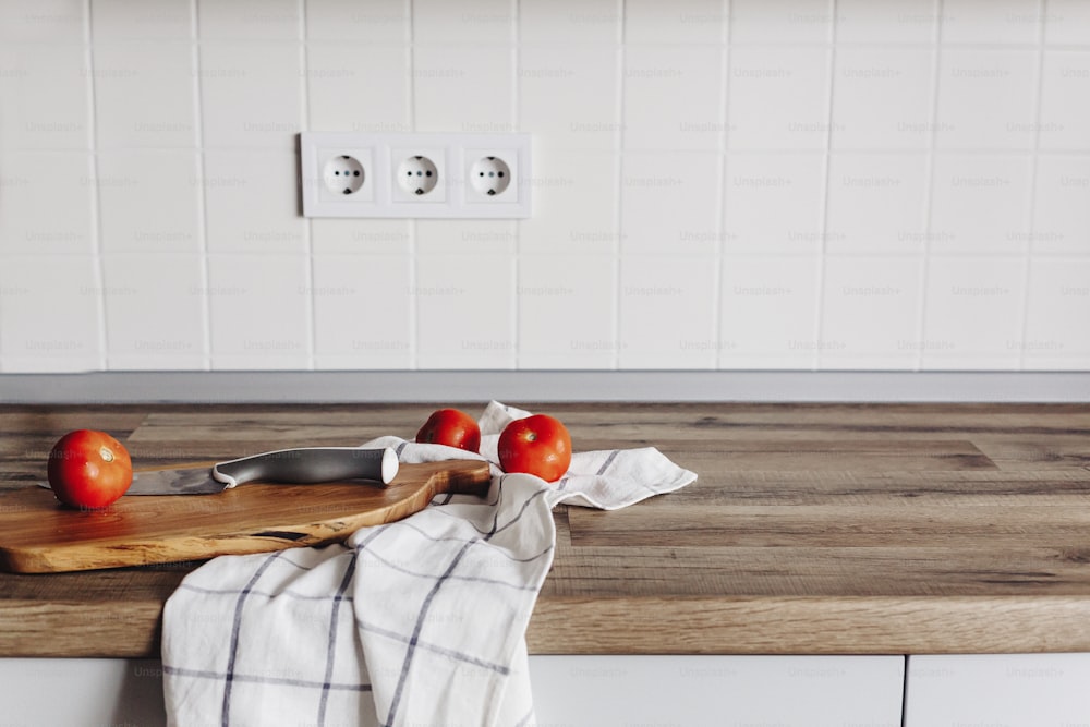 Cucinare il cibo su una cucina moderna, coltello su tagliere di legno con verdure, spezie su tavolo di legno. Cibo fatto in casa. Eleganti mobili da cucina in colore grigio in stile scandinavo.