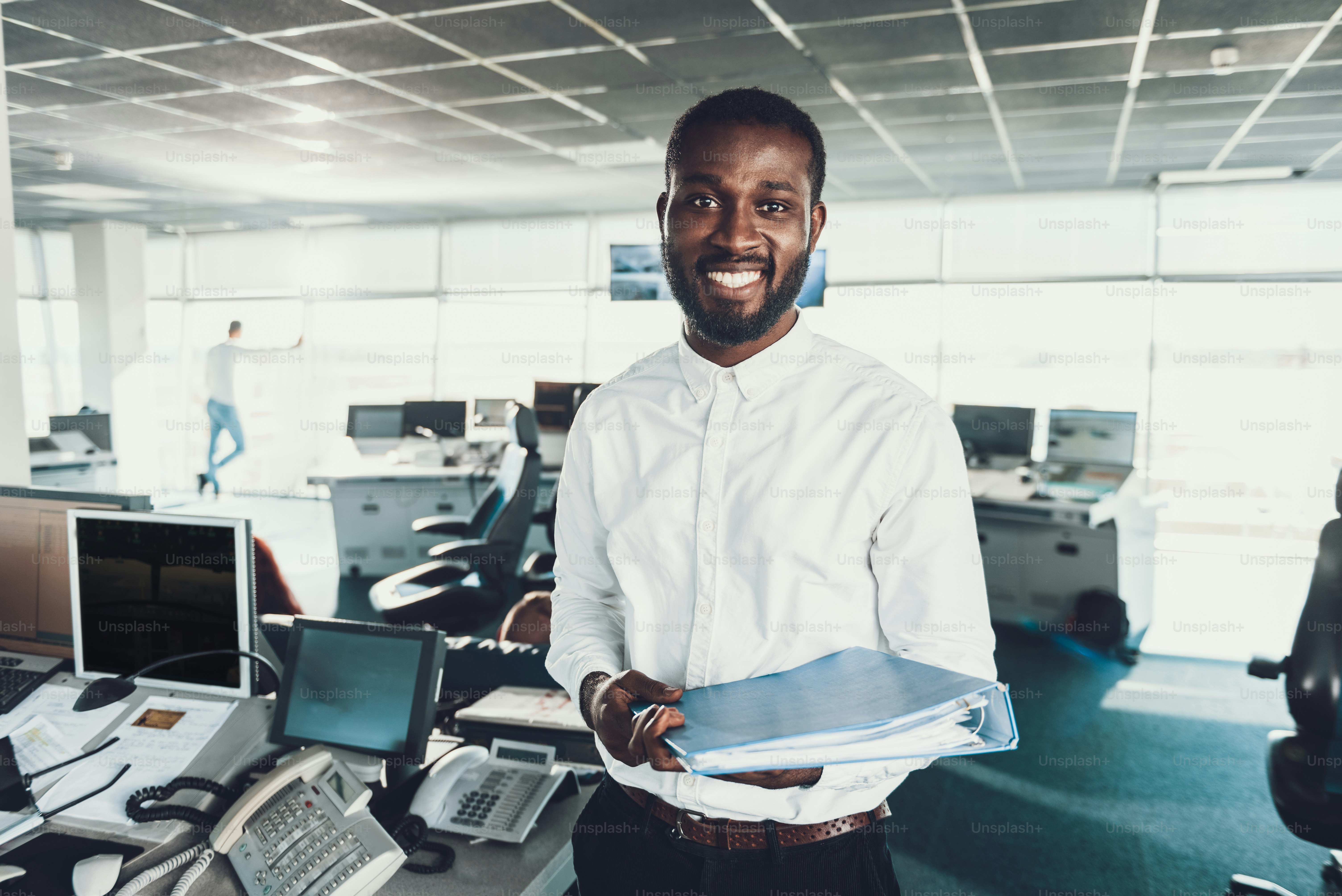 Waist up portrait of smiling afro-american man holding documents folder in hands while staying in office room