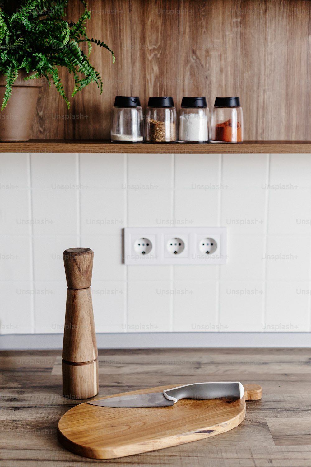 Modern knife on wooden cutting board with pepper spice on wooden table top. Cooking on modern kitchen with furniture in grey color. Gray cabinets in scandinavian style and wood. Home food