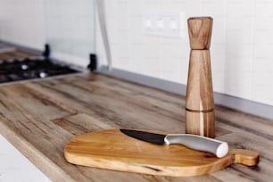 木製のまな板にモダンなナイフ、木製のテーブルの上にペッパースパイス。グレーの家具を備えたモダンなキッチンで調理します。スカンジナビアスタイルのグレーのキャビネット。家庭料理