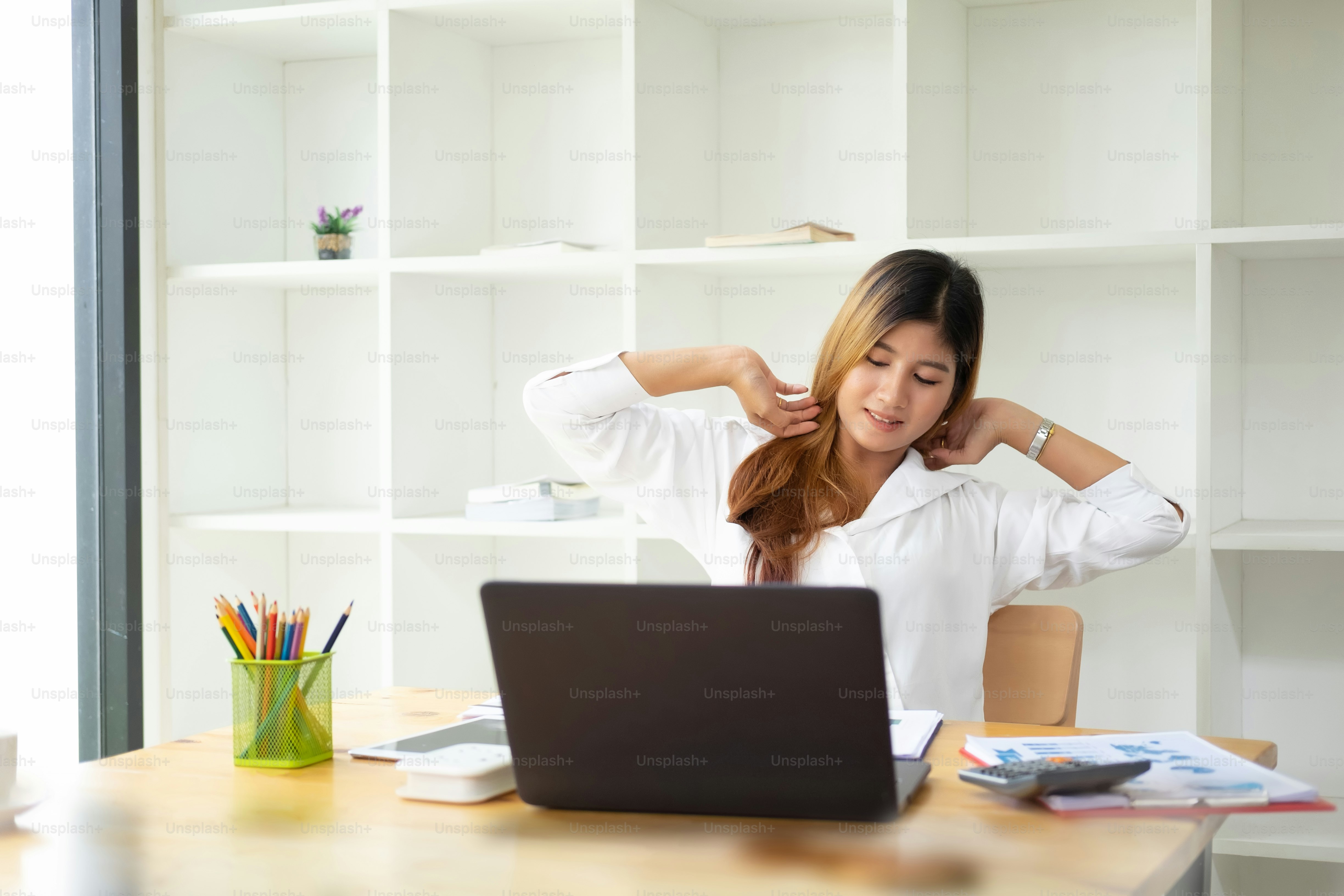 椅子でリラックスする実業家は、仕事が終わった後に満足してオフィスで休んでいる幸せなアジアの女性を手にします。