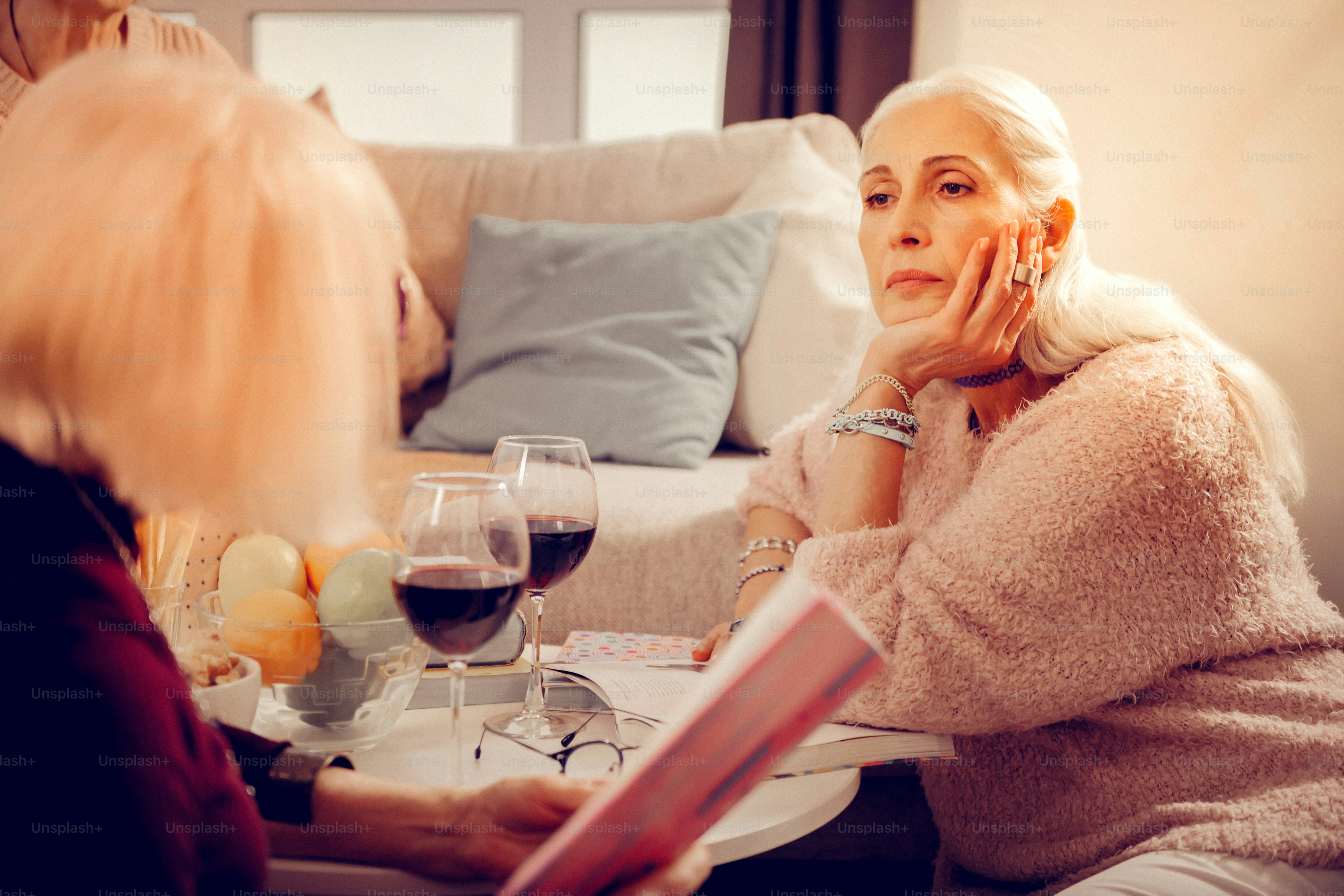 Belle poésie. Belle femme rêveuse regardant le verre de vin tout en écoutant son ami