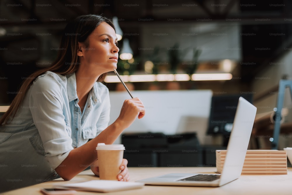 Side view portrait of thoughtful girl leaning on office desk with white  notebook. She is holding cup of coffee and touching chin with pencil photo  – One woman only Image on Unsplash