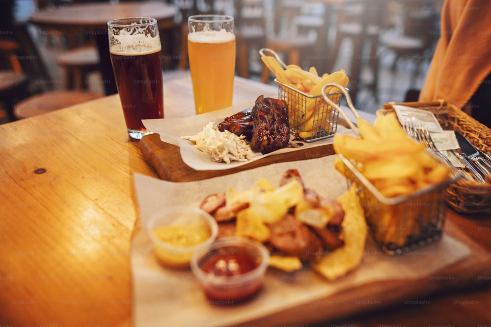 Deliziosa salsiccia affumicata con patatine fritte, patatine fritte e bistecca con salsa su tavola di legno. concetto festivo di fast food di strada. carne arrosto e bevande fredde alla birra.