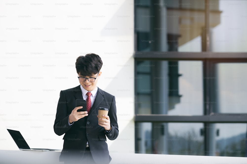 Junger Geschäftsmann, der Handy-Apps außerhalb des Büros mit Wolkenkratzern im Hintergrund SMS schreibt. Junger Mann mit Smartphone für geschäftliche Arbeit.