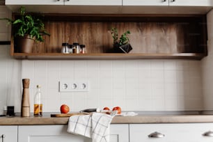 회색 색상의 가구와 나무 테이블 상판으로 현대적인 주방에서 음식을 요리합니다.  야채, 후추, 향신료와 나무 도마에 칼. 스칸디나비아 스타일의 세련된 주방 인테리어