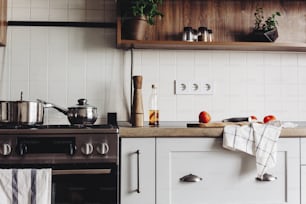 Kochen von Speisen in moderner Küche mit Stahlofen, Töpfen, Messer auf Holzschneidebrett mit Gemüse, Pfeffer, Gewürzen, Öl auf Holztischplatte. Essen zu Hause. Stilvolle Küchenmöbel in grauer Farbe
