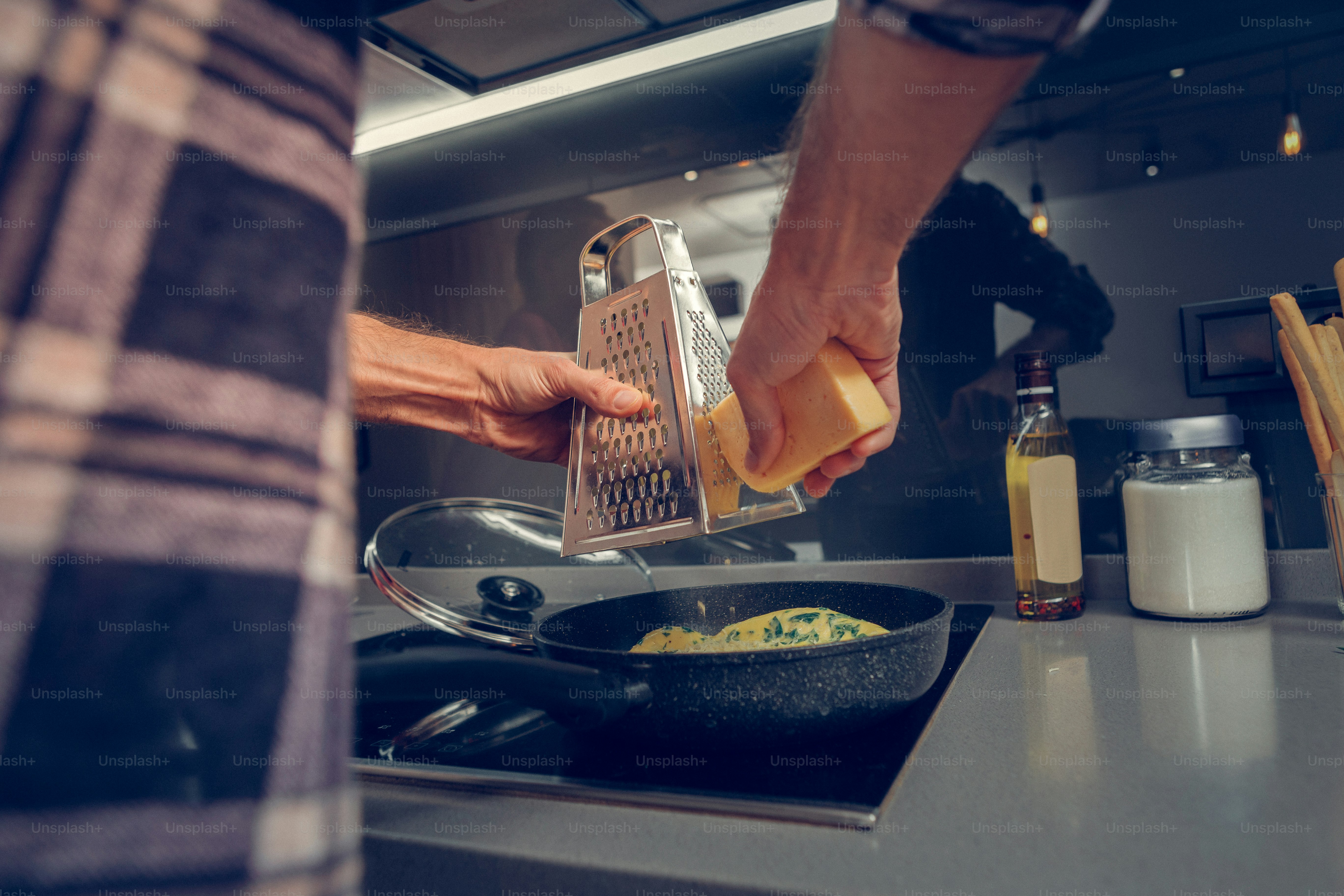 Cheese. Tall man wearing a checkered shirt grating cheese on the omelet while cooking in the kitchen