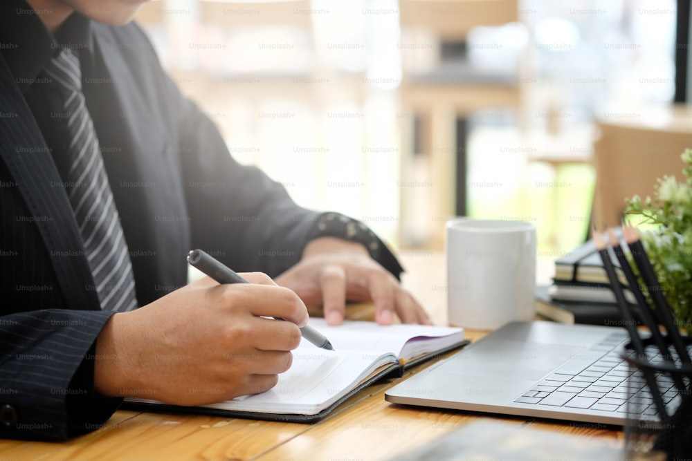 Cropped image of hand of businessman writing notes on desk at office