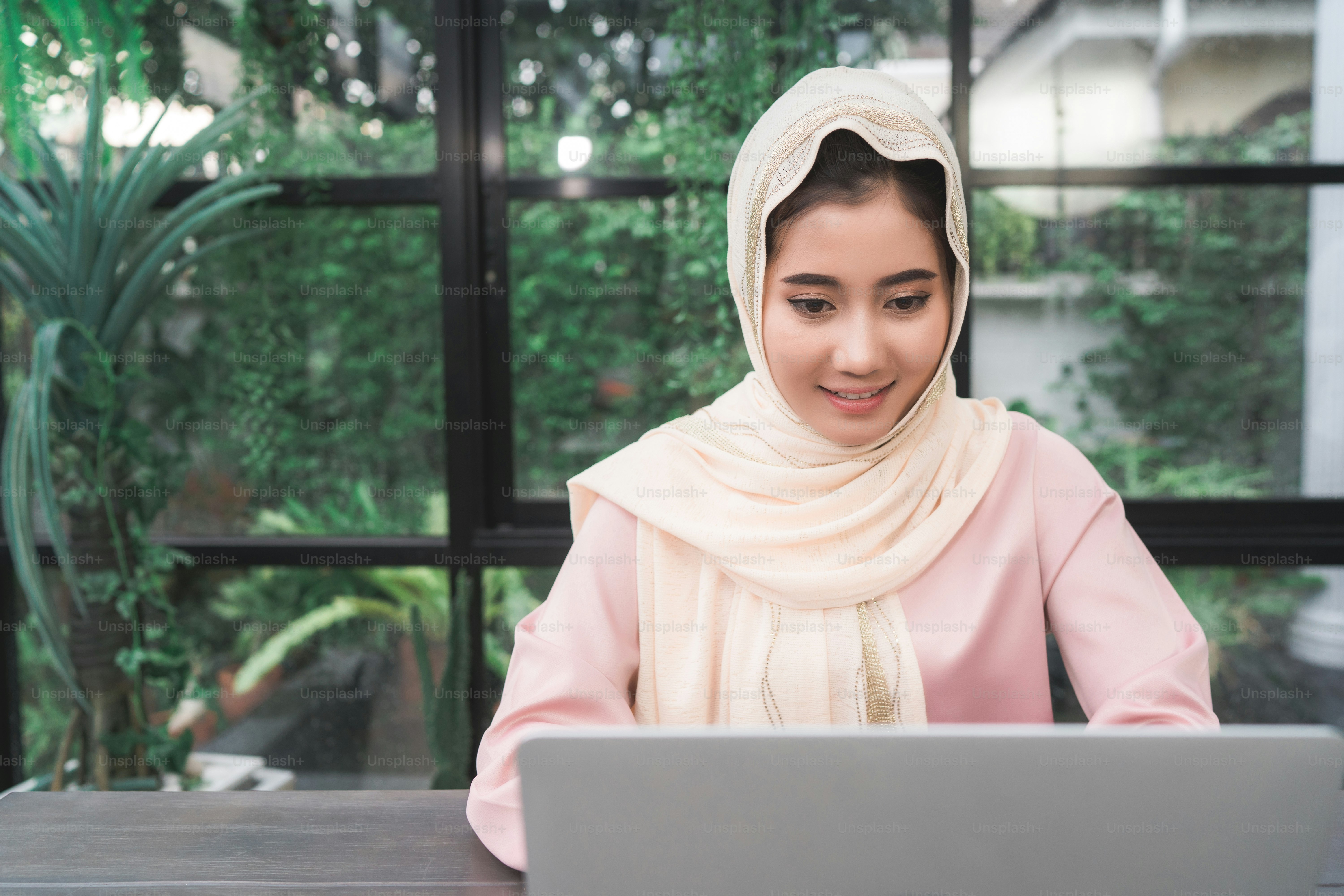 Beautiful young smiling asian muslim woman working on laptop sitting in ...