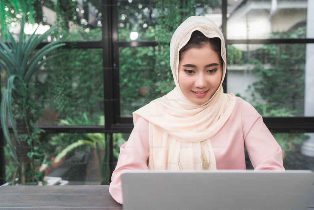 Beautiful young smiling asian muslim woman working on laptop sitting in living room at home. Asian business woman working document finance and calculator in her home office. Enjoying time at home.
