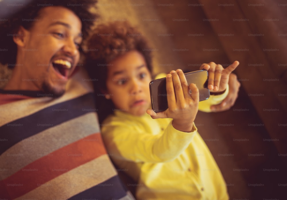Tendremos recuerdos maravillosos y divertidos. Padre e hija afroamericanos tomándose una foto con el teléfono. Cerrar. Concéntrate en las manos.