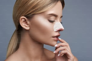 Calm young lady thoughtfully looking down while touching her nose with white strip