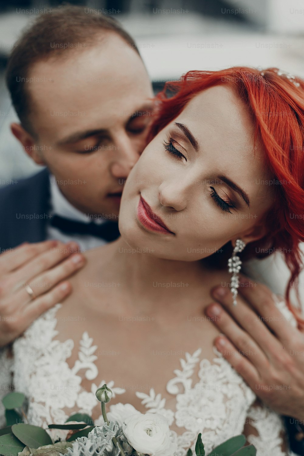 stylish groom gently kissing his happy bride in neck at retro car and smiling. emotional romantic moment, space for text. luxury wedding newlyweds couple embracing