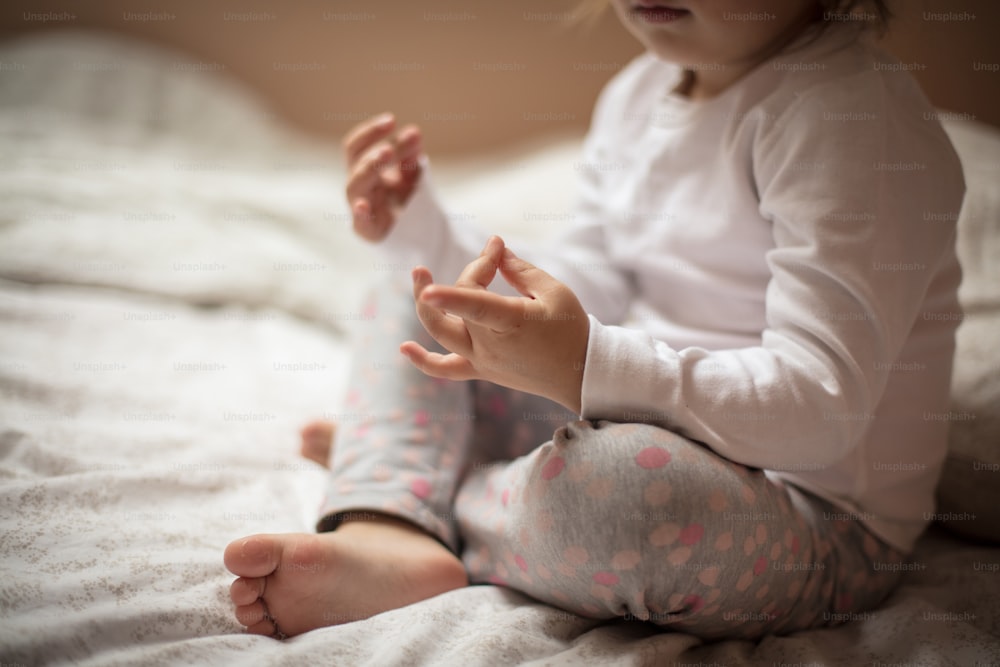 He knows how to calm her energy. Little girl working yoga on bed. Close up. Focus on hand.
