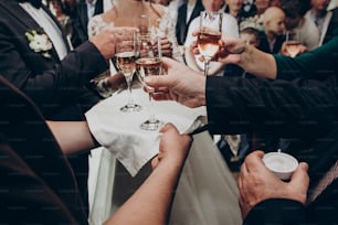 hands holding glasses of champagne. stylish happy wedding couple toasting with family, celebrating wedding. space for text. luxury life and wedding reception. expensive catering