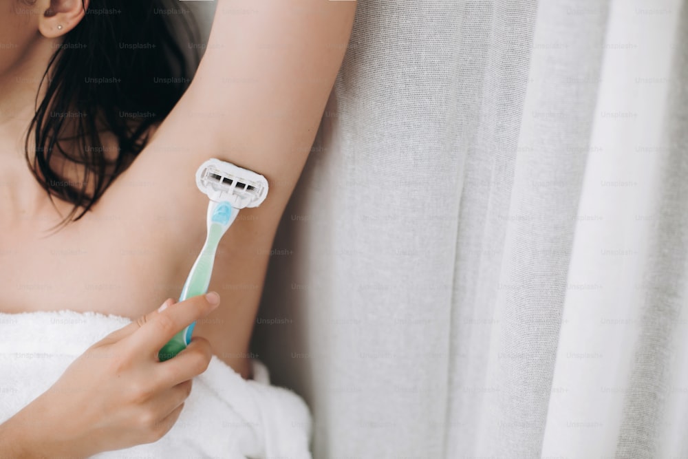 Hand holding plastic razor and shaving smooth armpit. Young woman shaving armpits with plastic razor closeup in home bathroom. Skin care. Hair Removal concept. Copy space.