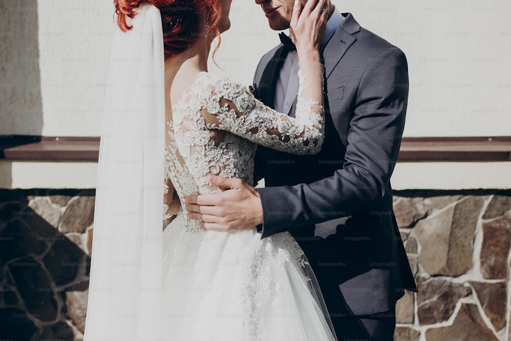 Stilvolle glückliche Braut und Bräutigam, die sich bei der Hochzeitszeremonie vor dem Hintergrund der Kirche umarmen. Emotionaler Moment, Raum für Text. Luxushochzeit Brautpaar