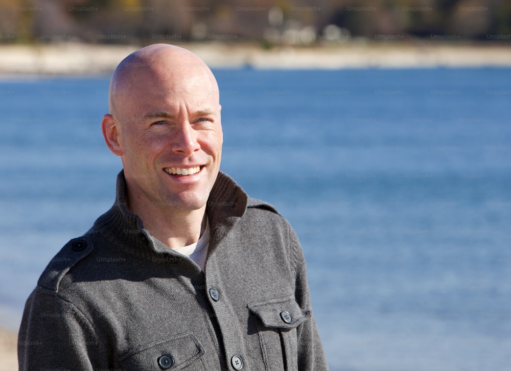 a bald man standing in front of a body of water
