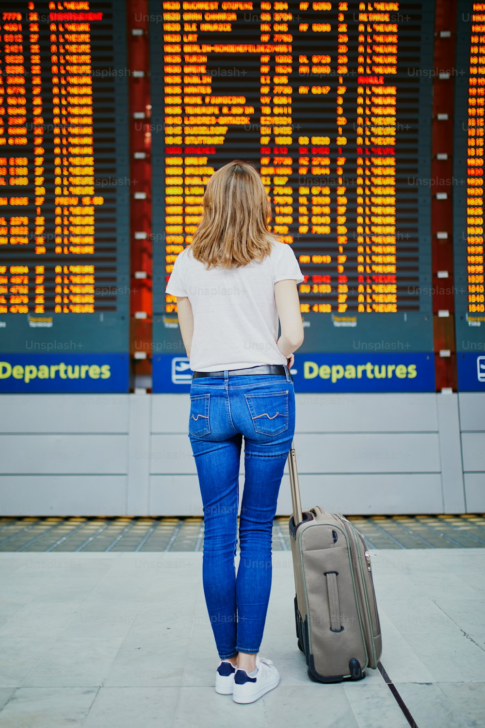 Mulher nova no aeroporto internacional com bagagem perto da exibição da informação do voo