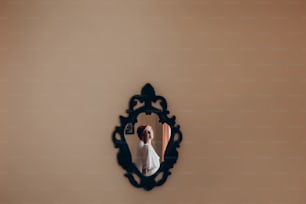 happy stylish bride in silk robe looking in mirror on the wall and smiling.  rustic wedding morning preparation. portrait reflection of young woman. space for text. luxury bride