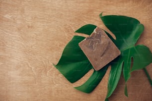 Natural soap on wooden background with green monstera leaf. Plastic free beauty essentials. Zero waste concept, flat lay with copy space. Sustainable lifestyle