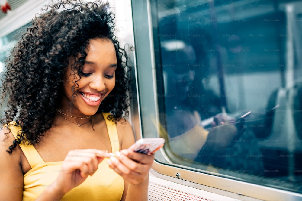 Young black woman sitting inside the underground on the mobile phone