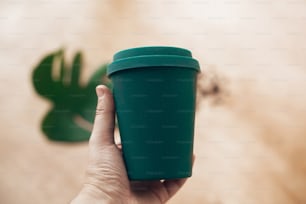 Ban single use plastic. Hand holding eco reusable coffee cup on wooden background. Coffee cup from bamboo fiber, zero waste concept.  Take away coffee in your cup. Sustainable lifestyle