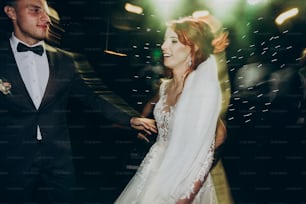 happy bride and stylish groom dancing at wedding reception. gorgeous wedding couple having fun and partying in restaurant in light show. newlywed emotional moment. space for text