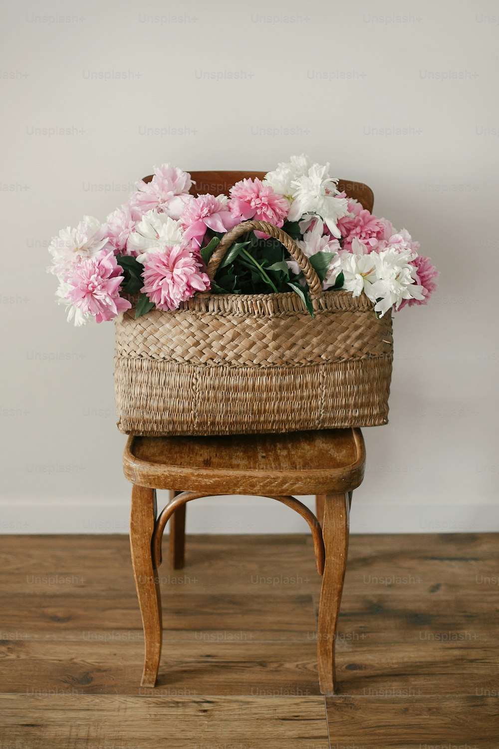 Elegantes peonías rosas y blancas en bolsa de paja en silla rústica de madera en la habitación. Día Internacional de la Mujer. Feliz día de la madre. Hola primavera. Hermoso ramo. Vida en el campo