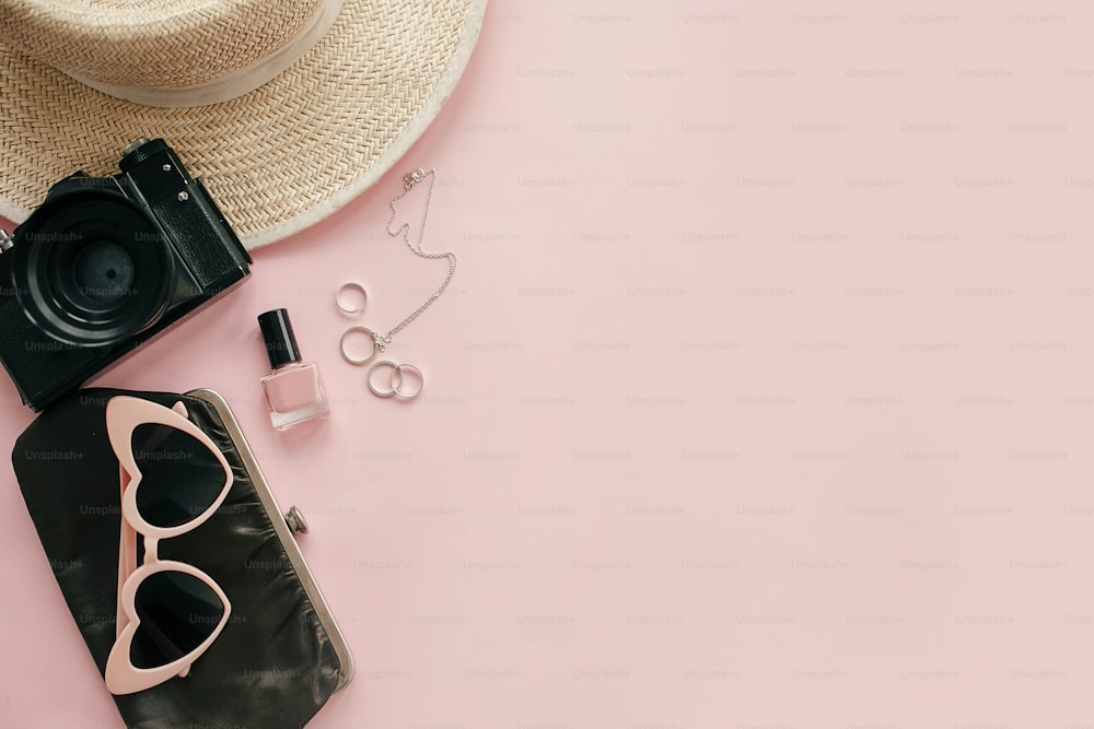 International Women's Day flat lay. Stylish girly image of photo camera, retro sunglasses, jewelry, nail polish, hat, purse on pastel pink paper with copy space.  Hello spring concept.