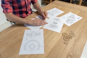 Profile side view of clever and focused man sitting behind wooden desk in loft interior and making engendering drawing, measure distant thinking about result