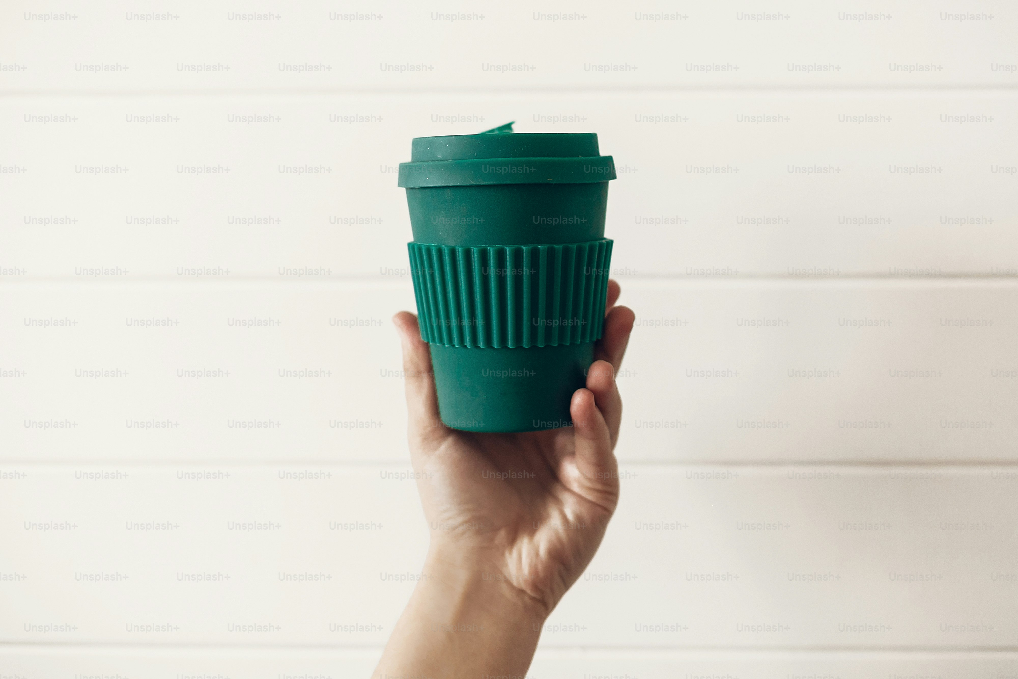 Zero waste concept. Hand holding stylish reusable eco coffee cup on white wooden background. Green Cup from natural  bamboo fiber. Ban single use plastic. Make a choice.